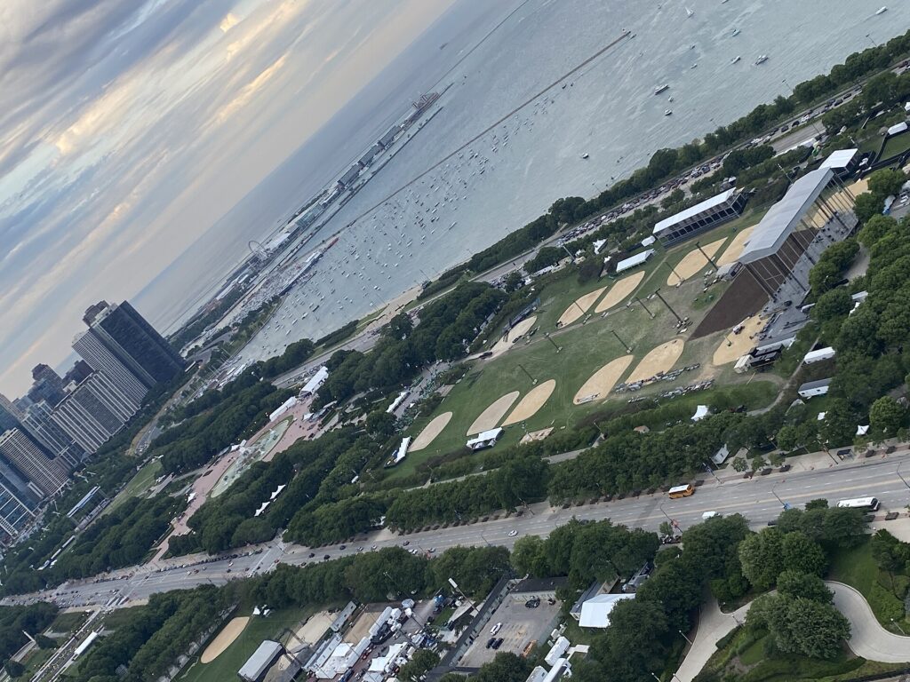 Festival crowd seen from above at a lakefront city park, large stage and skyline in the background