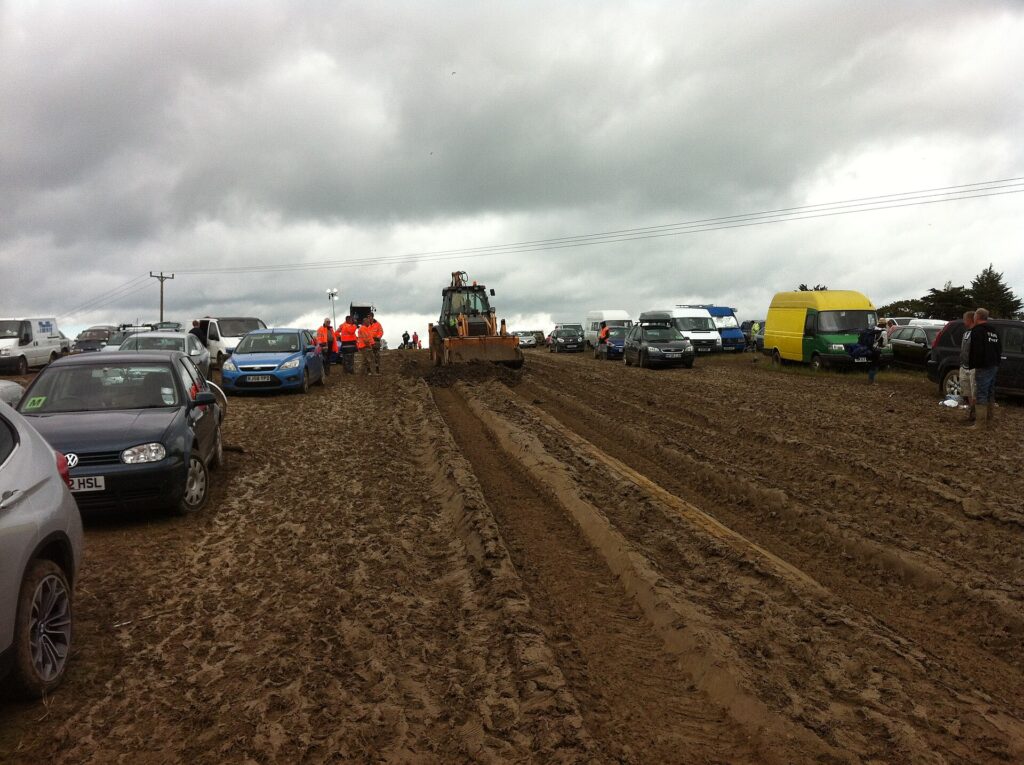 Festivalgoers in ponchos and gumboots standing in a muddy field