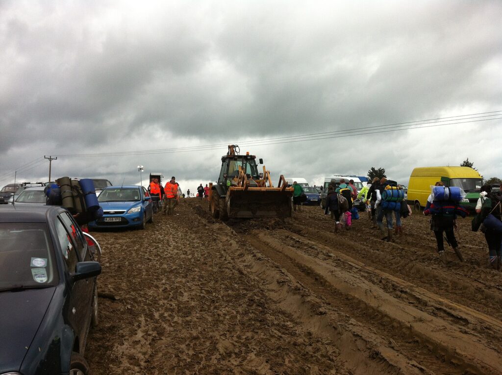 Festivalgoers in ponchos and boots on a muddy campsite path