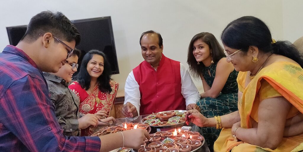 A family lighting clay diyas on a balcony, with a lit street below