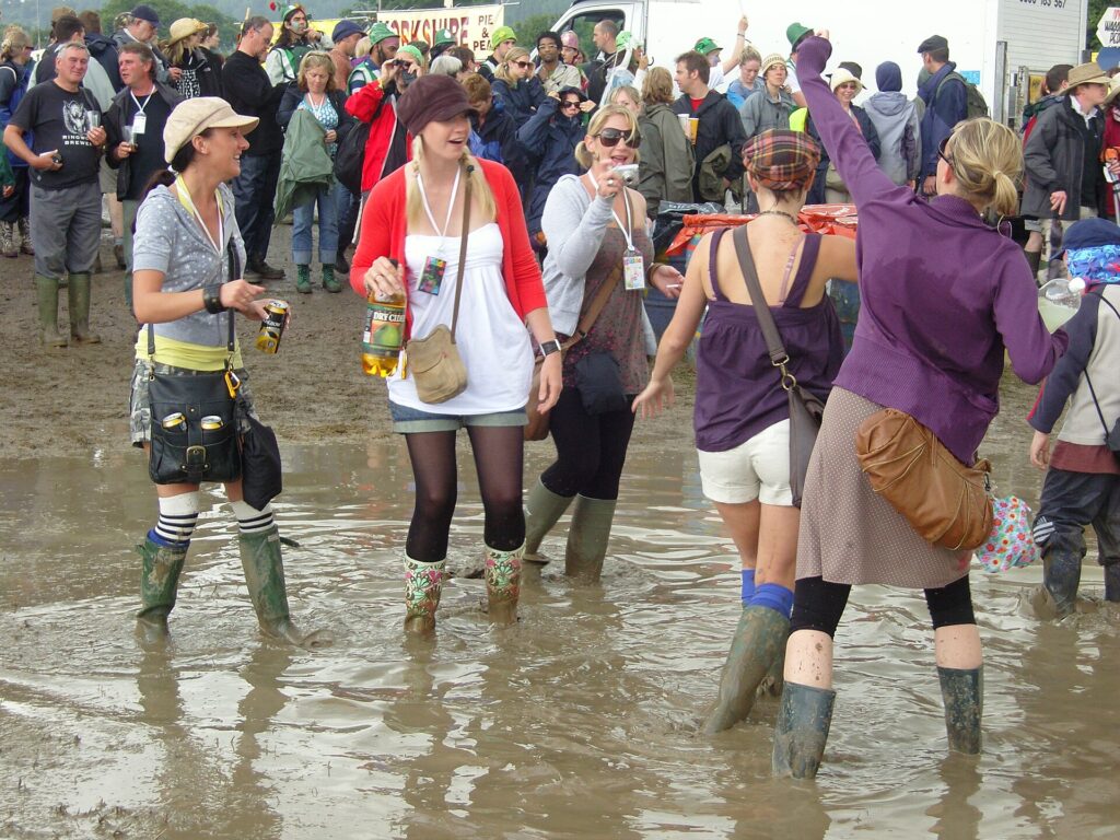 Muddy festival ground with wellington boots and rain clouds over a stage field