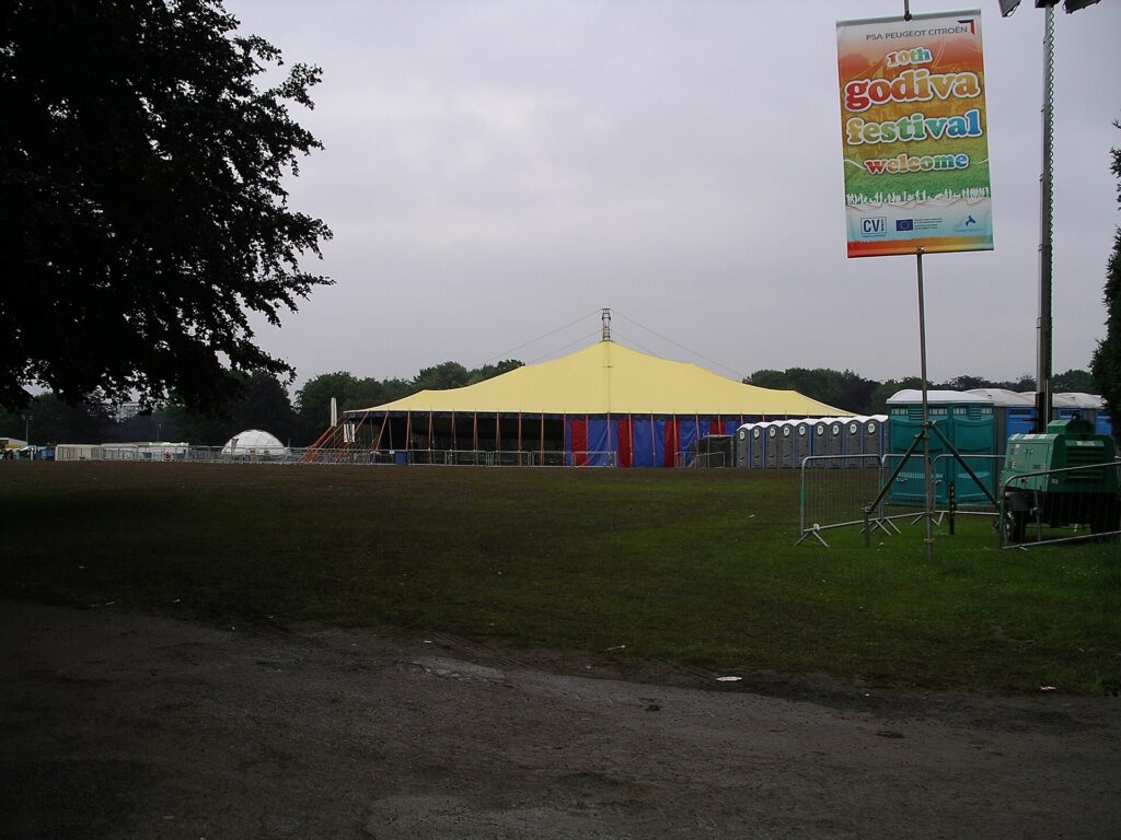 A small one-person tent pitched on a festival campsite beside a walkway