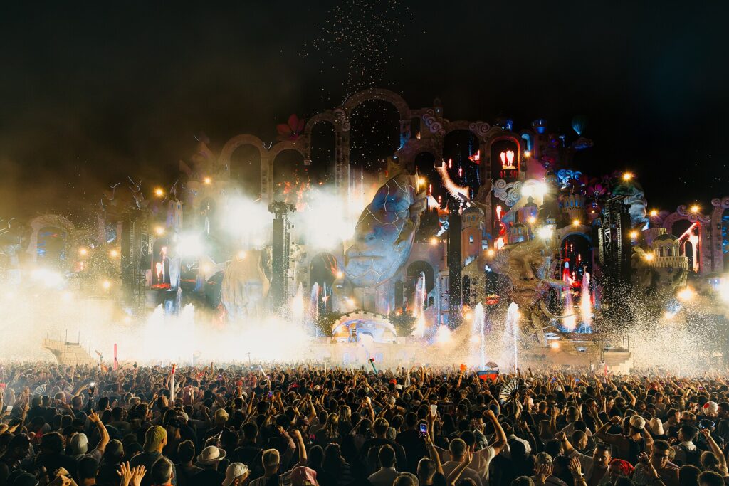 Main stage crowd at dusk during a large summer dance festival, wide shot from the field