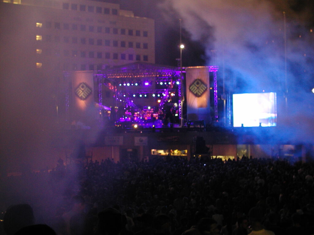 Crowd watching the main stage at a large outdoor music festival at dusk